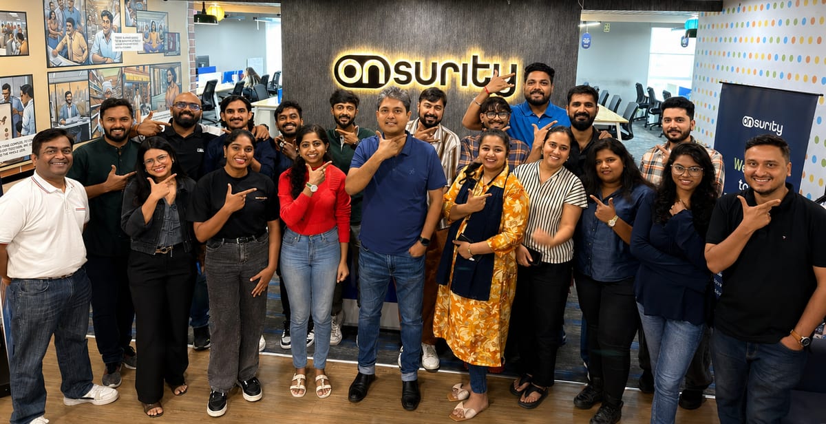 The Onsurity team together at the office, pointing at the glowing Onsurity logo — life at Onsurity