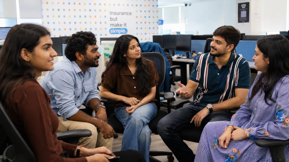 Onsurity teammates in a huddle in front of the “Insurance but make it simple” wall at the office